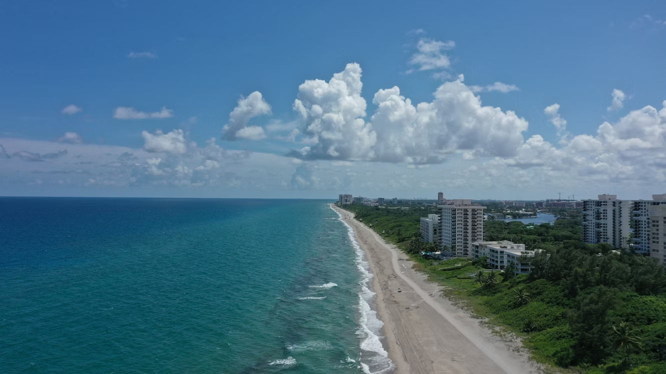 Aerial view of sandy beach with turquoise ocean and high-rise buildings along tropical coastline.