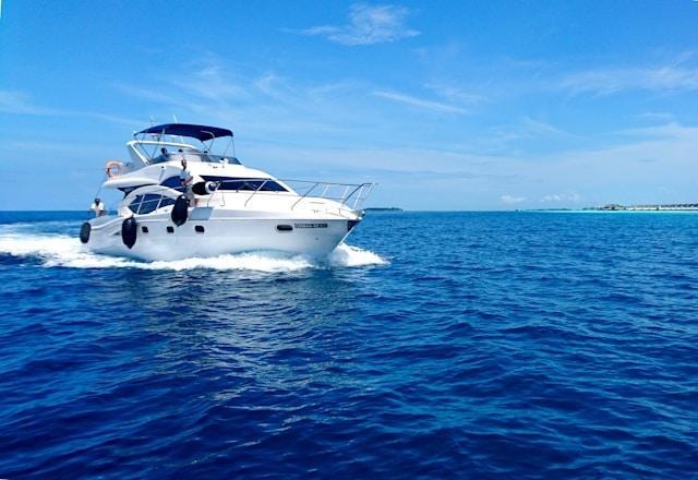 White private yacht cruising through blue ocean near shoreline on sunny day.