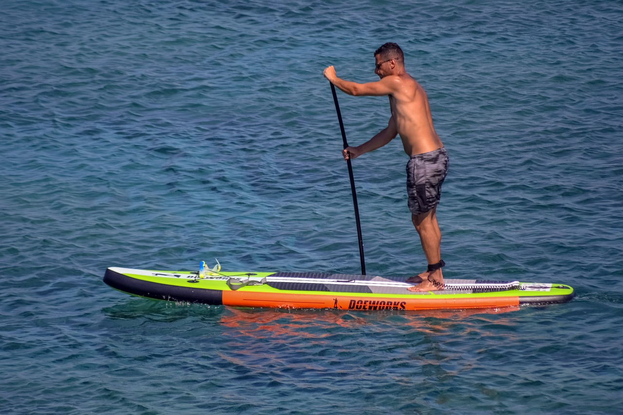 Man paddleboarding on a bright board over calm blue water.