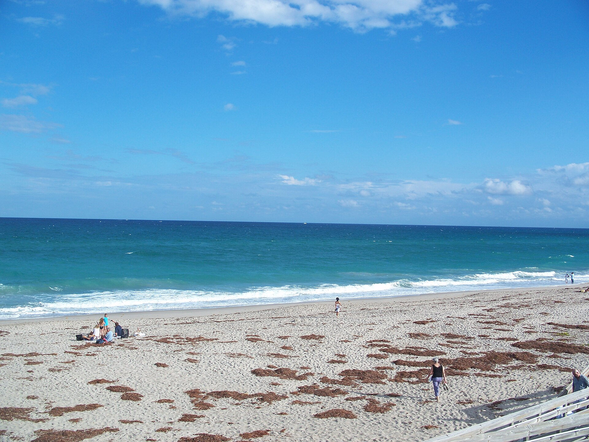 People walking along a sandy beach with turquoise ocean waves.
